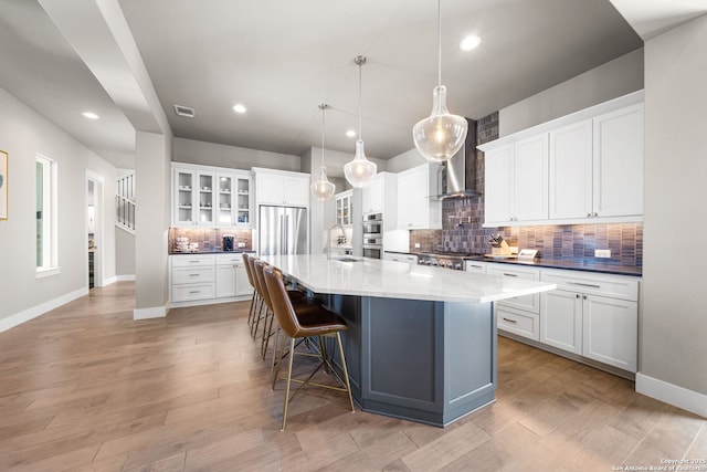 kitchen with light wood-style flooring, appliances with stainless steel finishes, white cabinetry, a sink, and wall chimney range hood