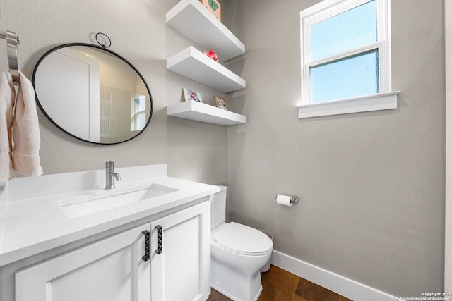 half bathroom with toilet, vanity, baseboards, and wood finished floors