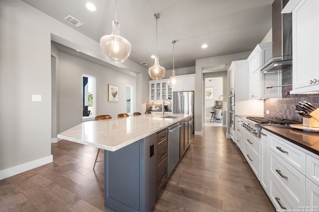 kitchen with visible vents, stainless steel appliances, wall chimney range hood, a kitchen bar, and a sink