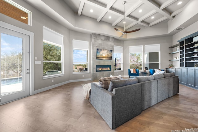 living area with visible vents, a towering ceiling, light wood-style floors, a tile fireplace, and coffered ceiling