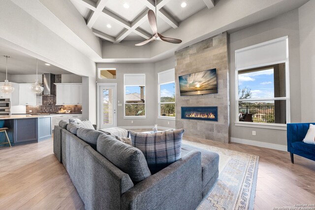 living area with a high ceiling, coffered ceiling, light wood-style floors, baseboards, and beam ceiling