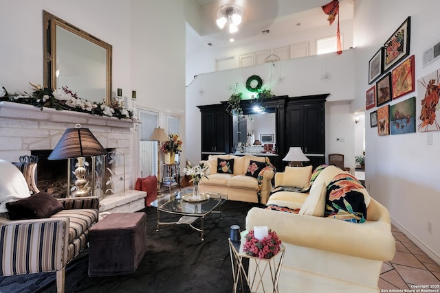 tiled living room featuring baseboards, a stone fireplace, and a towering ceiling