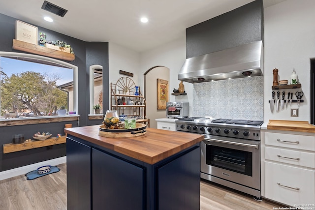 kitchen featuring high end stainless steel range oven, wall chimney exhaust hood, wood counters, and visible vents