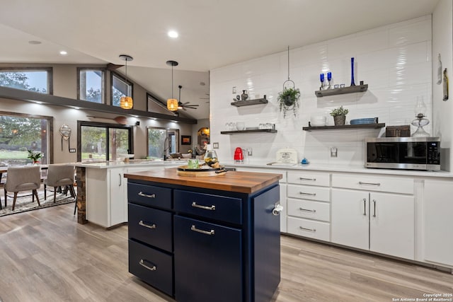 kitchen featuring open shelves, stainless steel microwave, light wood-style flooring, wood counters, and blue cabinets