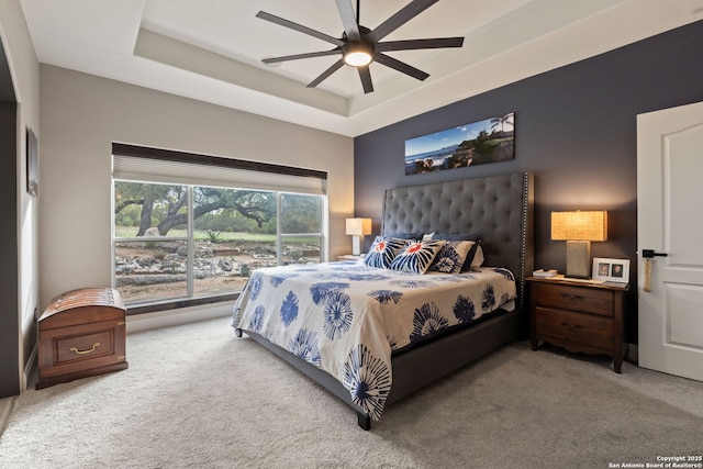 bedroom with a ceiling fan, a tray ceiling, and carpet flooring