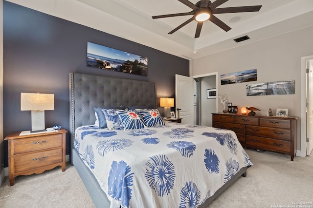 carpeted bedroom featuring a tray ceiling, visible vents, and a ceiling fan