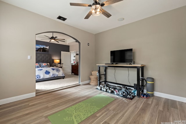 bedroom with arched walkways, wood finished floors, visible vents, and baseboards