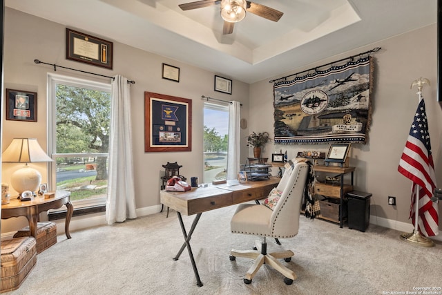 carpeted office space with a raised ceiling, a ceiling fan, and baseboards