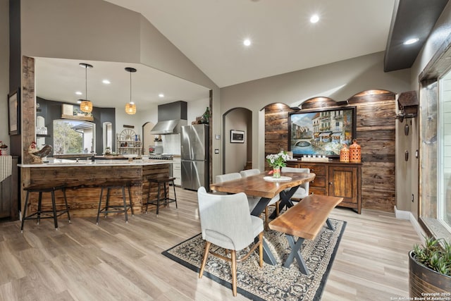 dining space with arched walkways, vaulted ceiling, light wood-type flooring, and recessed lighting