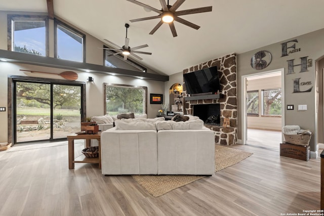 living area featuring light wood-style floors, ceiling fan, high vaulted ceiling, and a stone fireplace