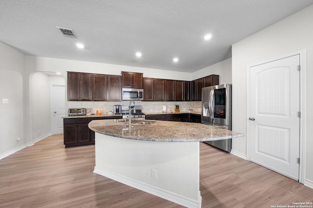 kitchen featuring stainless steel appliances, dark brown cabinetry, a center island with sink, and light wood-style floors