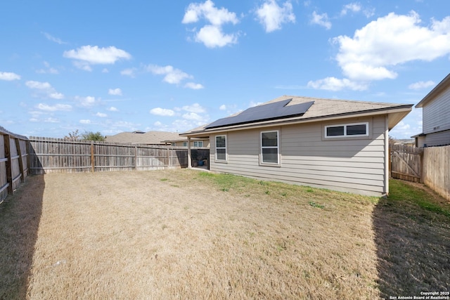 back of property featuring roof mounted solar panels, a fenced backyard, and a yard