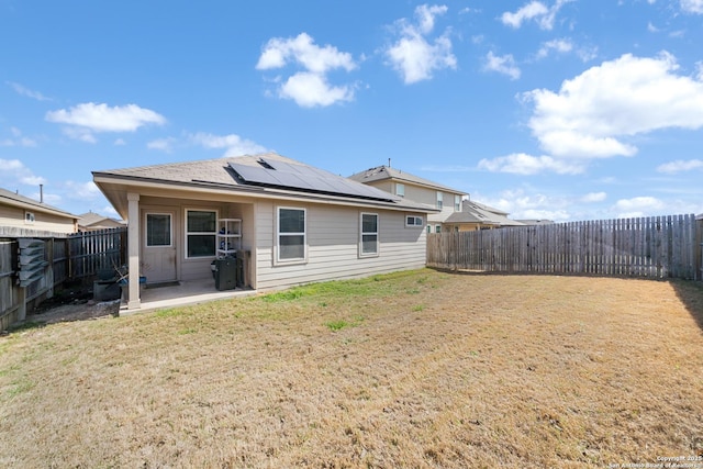 back of property with solar panels, a fenced backyard, a lawn, and a patio