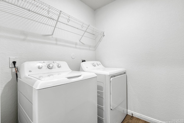 clothes washing area with washer and clothes dryer, a textured wall, wood finished floors, laundry area, and baseboards