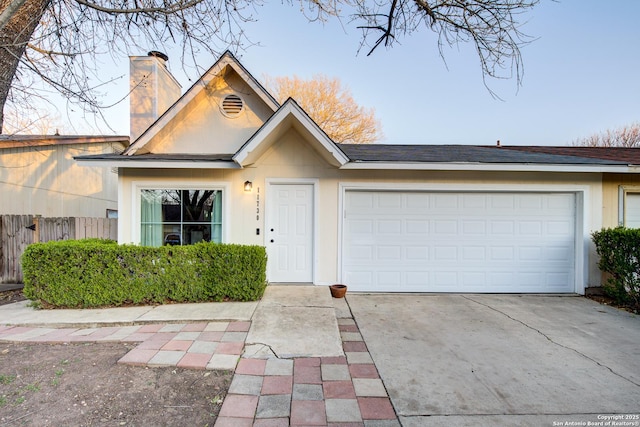 view of front of home featuring driveway, a chimney, an attached garage, and fence