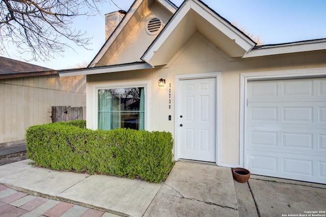 view of exterior entry featuring an attached garage and a chimney