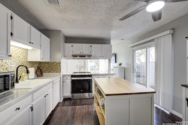 kitchen featuring dark wood-type flooring, butcher block countertops, a sink, visible vents, and appliances with stainless steel finishes