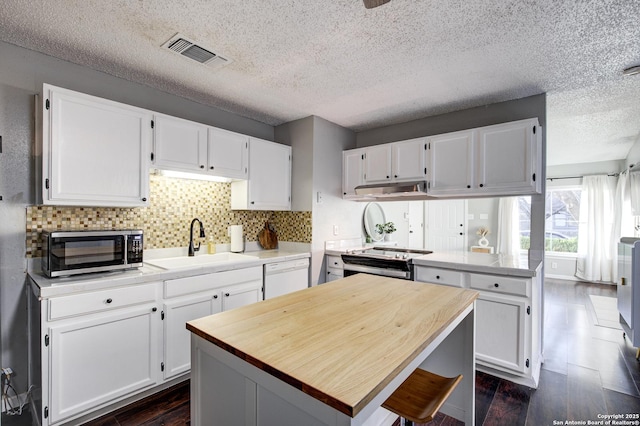 kitchen with visible vents, dark wood-style flooring, a peninsula, stainless steel appliances, and a sink