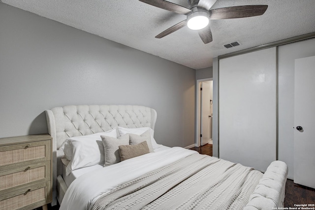 bedroom with visible vents, ceiling fan, dark wood-type flooring, a textured ceiling, and a closet