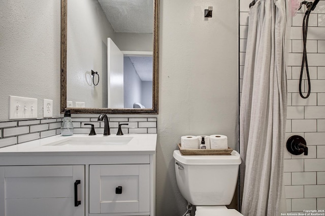 bathroom with a tile shower, vanity, toilet, and decorative backsplash