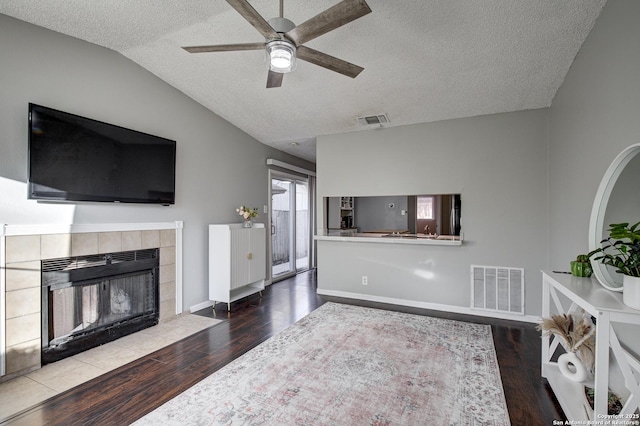 living area featuring lofted ceiling, visible vents, a fireplace, and wood finished floors