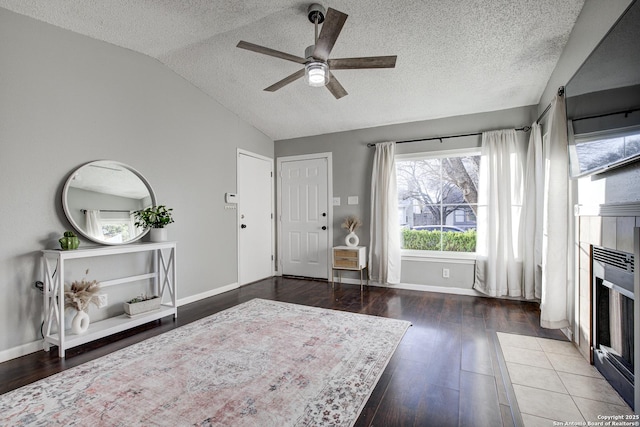 foyer entrance featuring lofted ceiling, a textured ceiling, a tiled fireplace, and wood finished floors