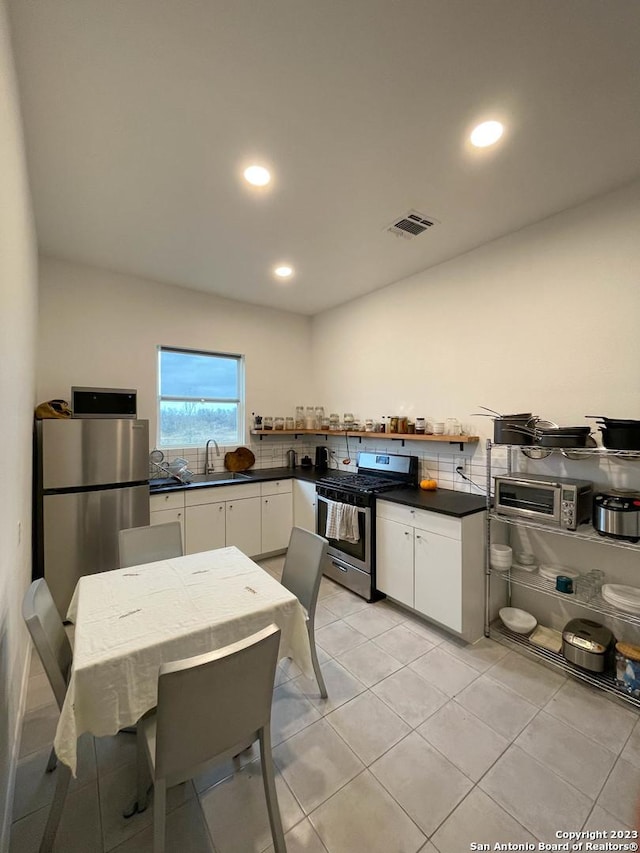 kitchen featuring appliances with stainless steel finishes, dark countertops, a sink, and white cabinetry