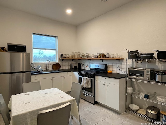 kitchen with open shelves, stainless steel appliances, dark countertops, white cabinetry, and a sink