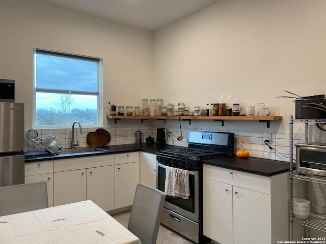 kitchen with stainless steel appliances, a sink, white cabinetry, open shelves, and dark countertops