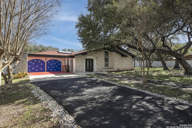 view of front of property with driveway, roof mounted solar panels, fence, and brick siding