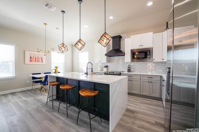 kitchen featuring tasteful backsplash, visible vents, wall chimney exhaust hood, appliances with stainless steel finishes, and light countertops