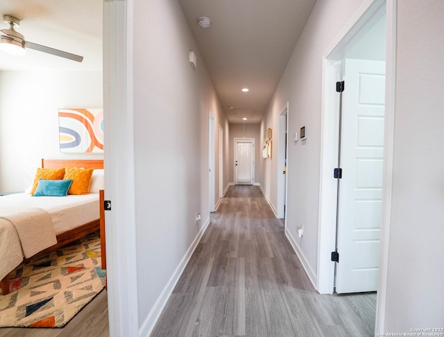 corridor featuring attic access, baseboards, wood finished floors, and recessed lighting