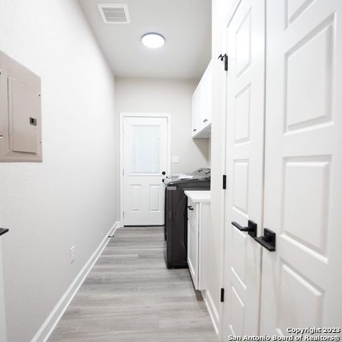 laundry area featuring cabinet space, electric panel, baseboards, visible vents, and light wood-style floors