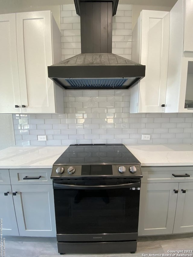 kitchen featuring light stone countertops, wall chimney exhaust hood, decorative backsplash, and electric range