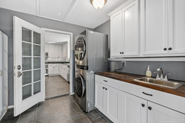 laundry room featuring cabinet space, attic access, stacked washer / drying machine, dark tile patterned floors, and a sink