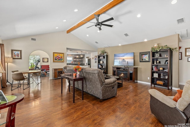 living room featuring a warm lit fireplace, visible vents, beam ceiling, and wood finished floors