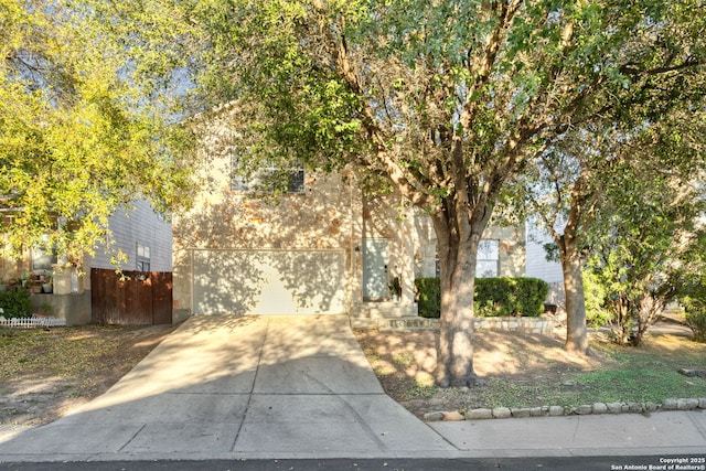 view of property hidden behind natural elements featuring a garage and concrete driveway