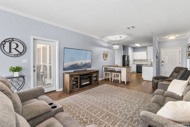 living room featuring crown molding, dark wood finished floors, visible vents, a glass covered fireplace, and baseboards