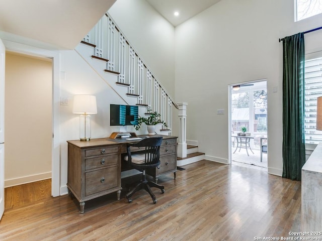 office area featuring light wood-type flooring, a high ceiling, and baseboards