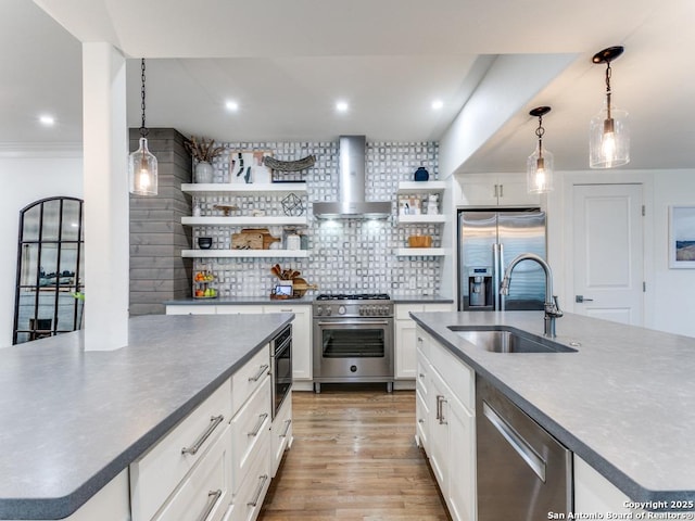 kitchen featuring an island with sink, wall chimney exhaust hood, open shelves, appliances with stainless steel finishes, and a sink
