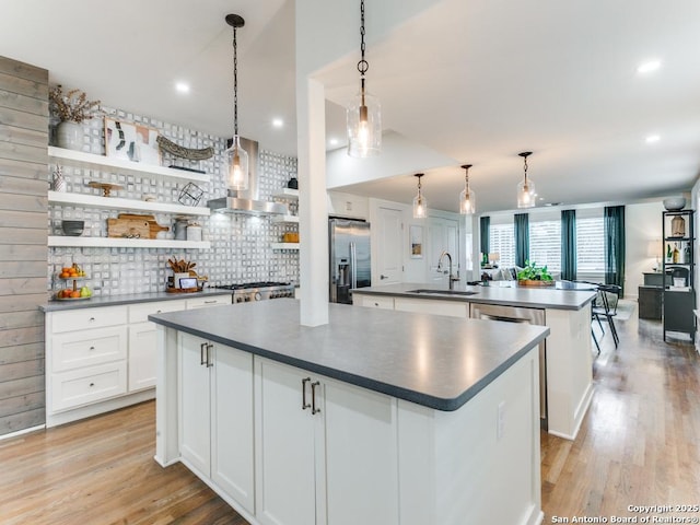 kitchen with an island with sink, wall chimney exhaust hood, tasteful backsplash, dark countertops, and stainless steel fridge