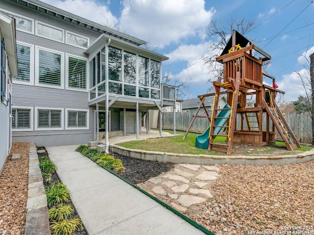 view of jungle gym with a sunroom, a patio, and fence