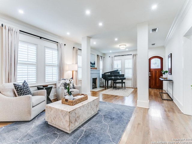living area featuring baseboards, a fireplace, crown molding, visible vents, and wood finished floors