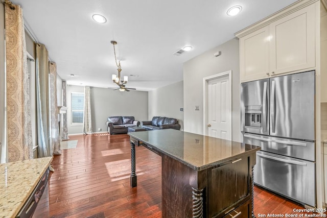 kitchen featuring open floor plan, dark stone counters, dark wood finished floors, and stainless steel fridge with ice dispenser