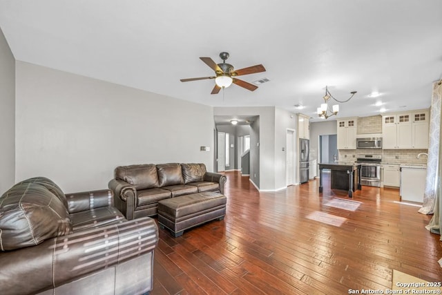 living room featuring ceiling fan with notable chandelier, hardwood / wood-style floors, visible vents, and baseboards