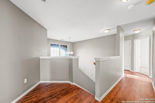 hallway with a chandelier, baseboards, an upstairs landing, and wood finished floors