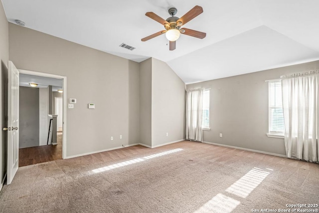 carpeted empty room with vaulted ceiling, baseboards, visible vents, and a ceiling fan