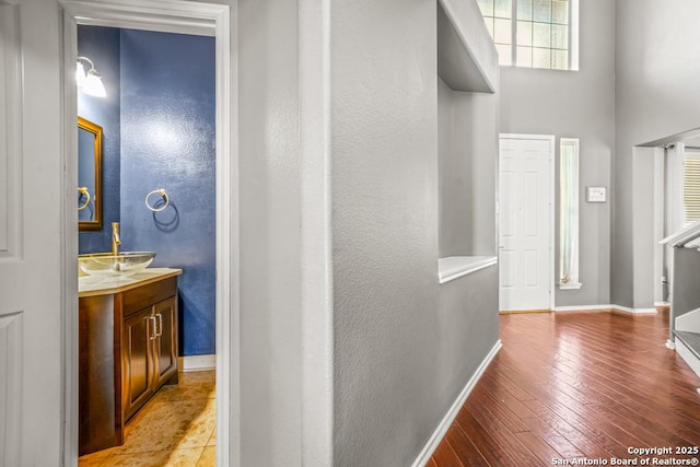 corridor with light wood-type flooring, baseboards, and a sink