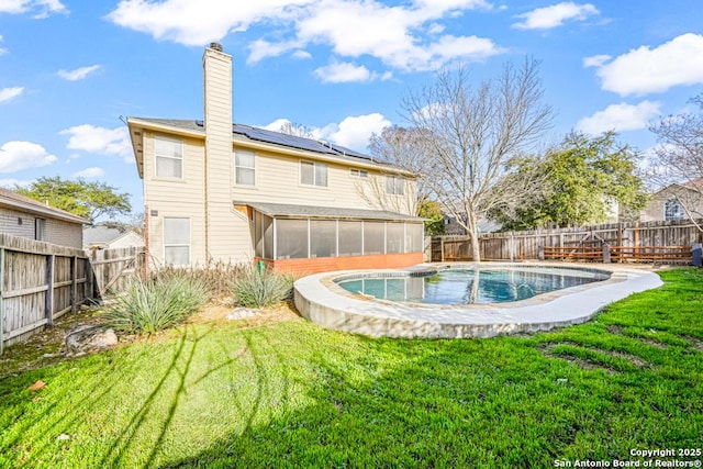 back of property with a sunroom, a fenced backyard, a lawn, and solar panels