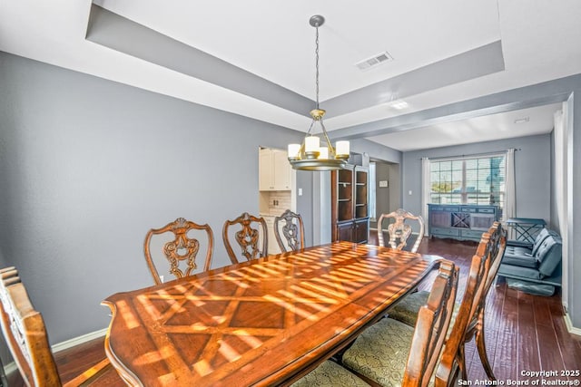 dining room featuring dark wood-style flooring, a raised ceiling, visible vents, and baseboards